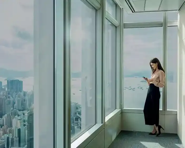 Woman standing comfortably beside floor-to-ceiling high-rise windows fitted with heat-control film overlooking a city skyline