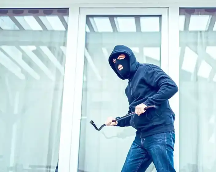 Masked intruder with a crowbar at a glass door held intact by safety window film