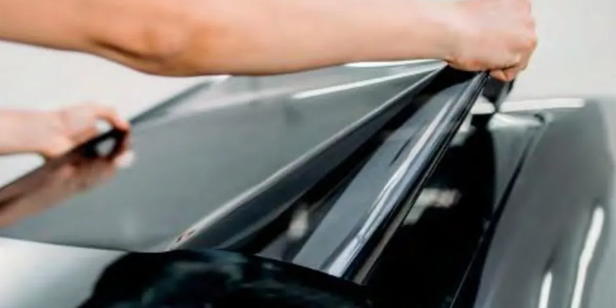 An installer laying a sheet of dark window film across a car windscreen