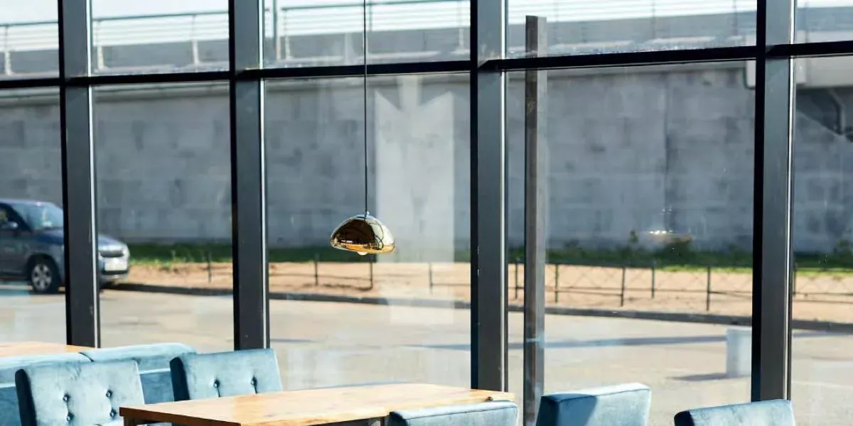 Upholstered chairs and a wooden table beside a full height glazed wall in strong daylight