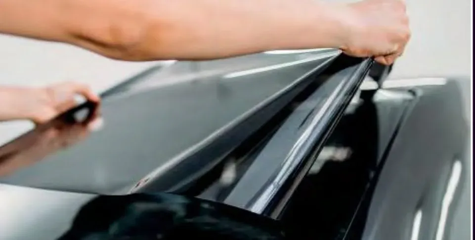 An installer lifting a cut sheet of tint film over a car window