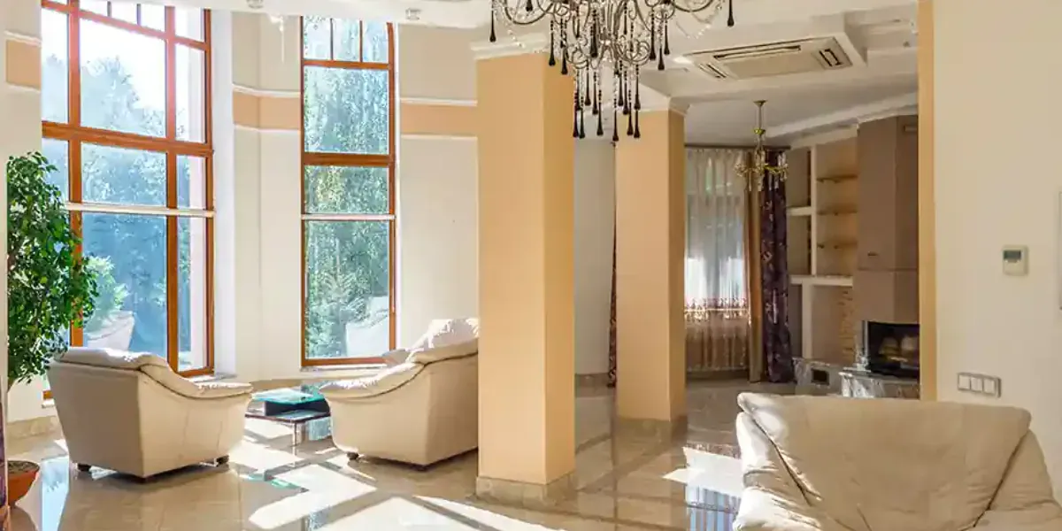 A living room with tall uncovered windows onto a garden, and heavy drawn curtains on a window in the room beyond
